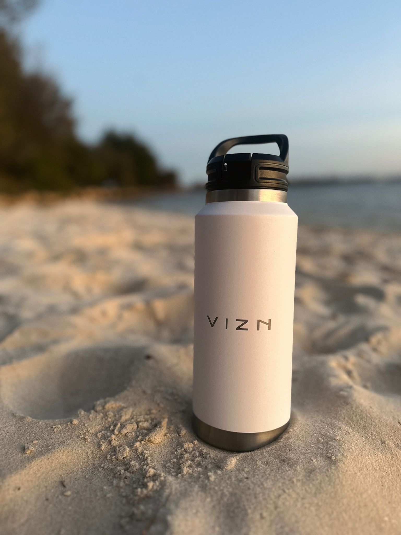 Snow white stainless steel water bottle with straw lid and carry handle on the sandy beach.